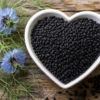 Black seed, powder, and oil on a kitchen counter alongside flatbread and roasted vegetables, illustrating Nigella sativa cardiovascular research.