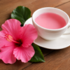 Deep red hibiscus tea in a glass teapot with three small cups on a sunlit wooden table, illustrating research on hibiscus and blood pressure.